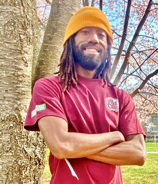 Intern Nick Jackson stands in front of a tree with his arms folded across his chest