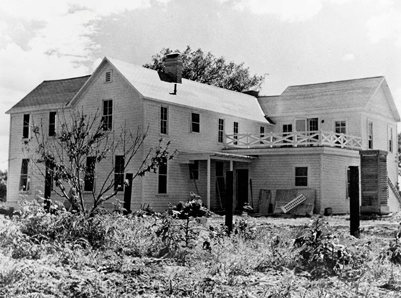 A two-story frame house with balcony and various construction materials propped against it.