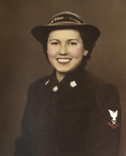 Sepia toned photo of a young woman smiling at the camera. She wears a dark uniform. Red trim is in color.