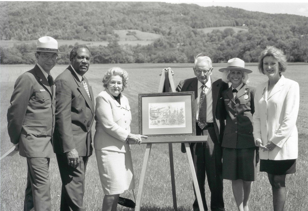 black and white photo of six people outside with a painting of mansion