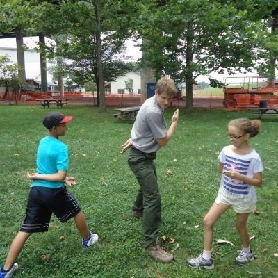 Park ranger with two youth playing the game "Ninja" in a grassy field.