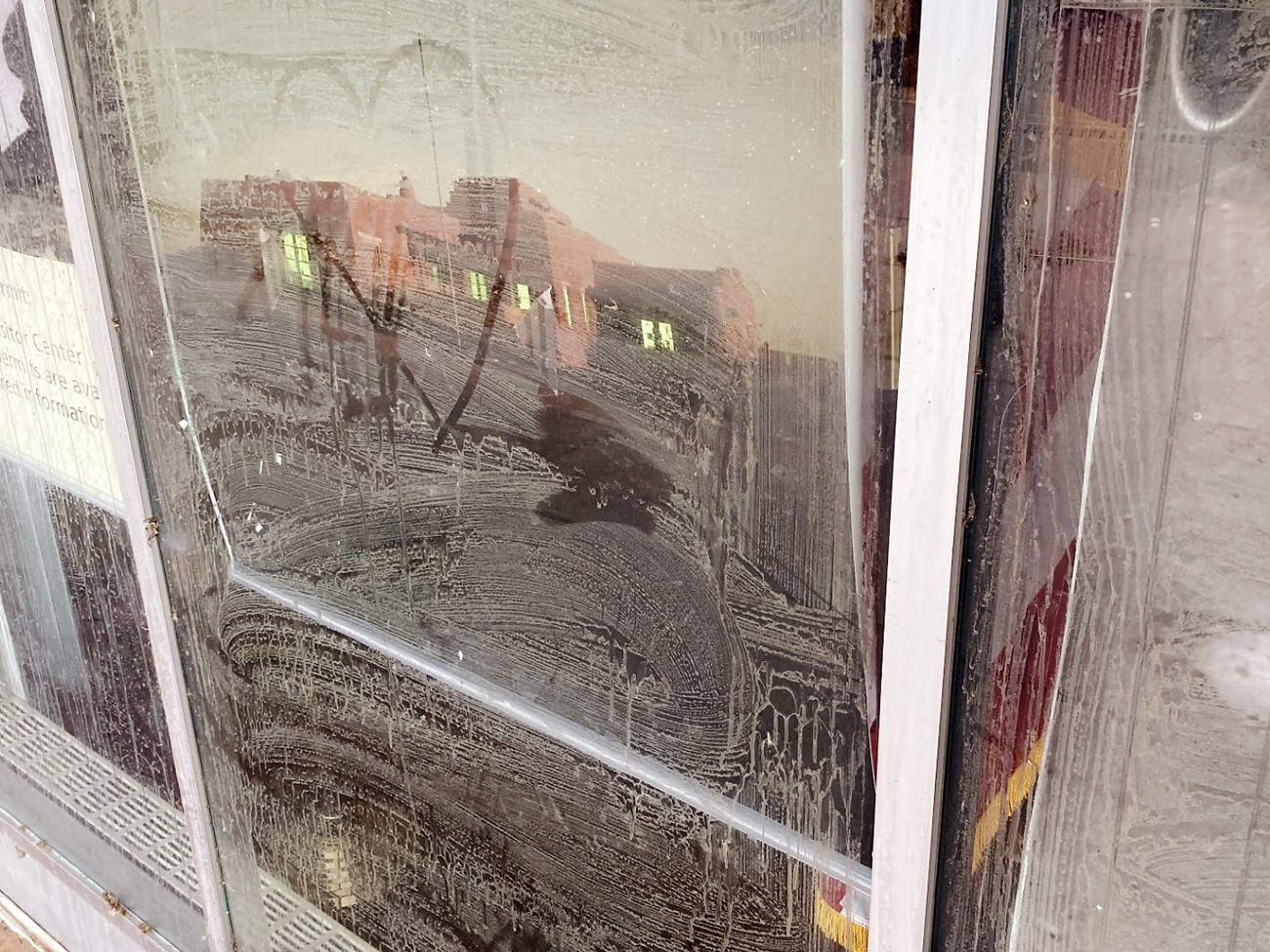 Window covered in what looks like dried, smeared, dirty water. Someone has drawn a heart through the soapy film with their finger. A stylish stucco building can be seen reflected in the dirty glass.