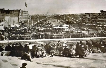 A black and white image of a large crowd gathered on city streets overlooking a parade