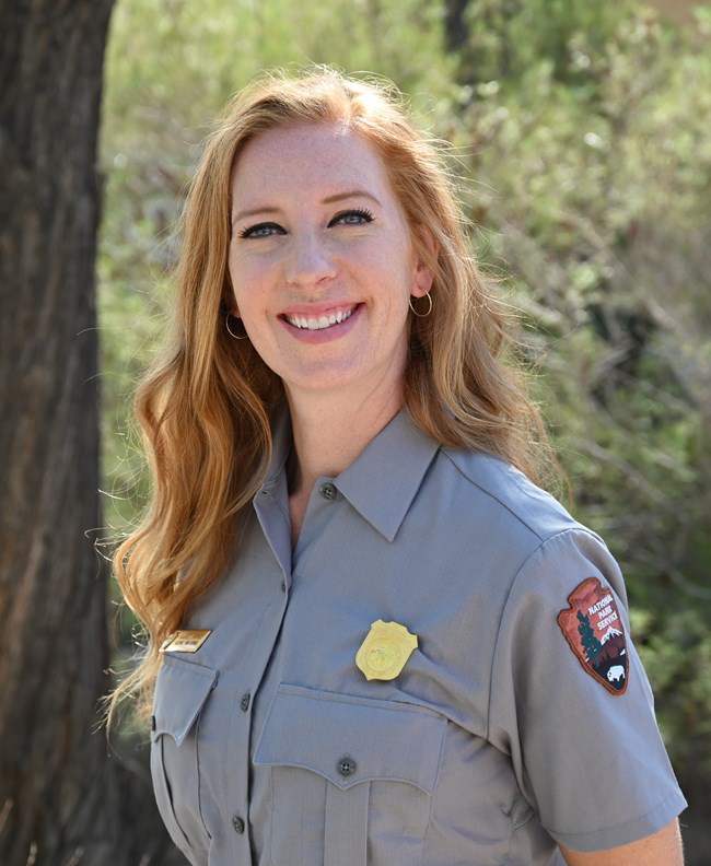 A woman with red hair smiles for a portrait, wearing a National Park Service uniform.