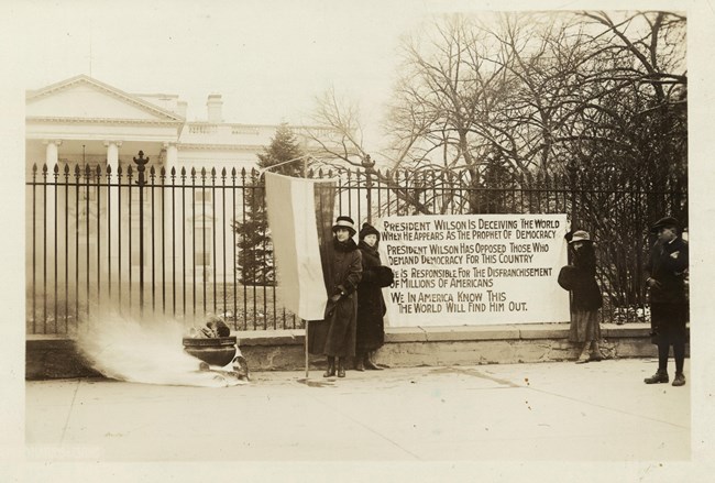 women stand outside the white house. Smoke comes from a black pot. Library of Congress