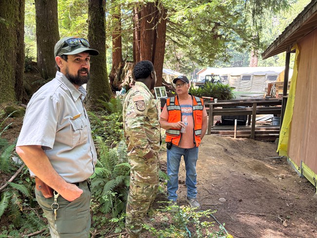 Patrick (left) stands in a wooded area with other workers