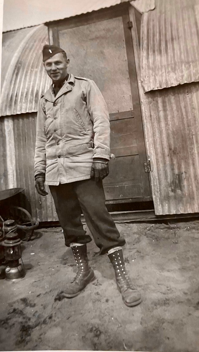 Young man in cold weather uniform standing in front of corrugated metal building and door.