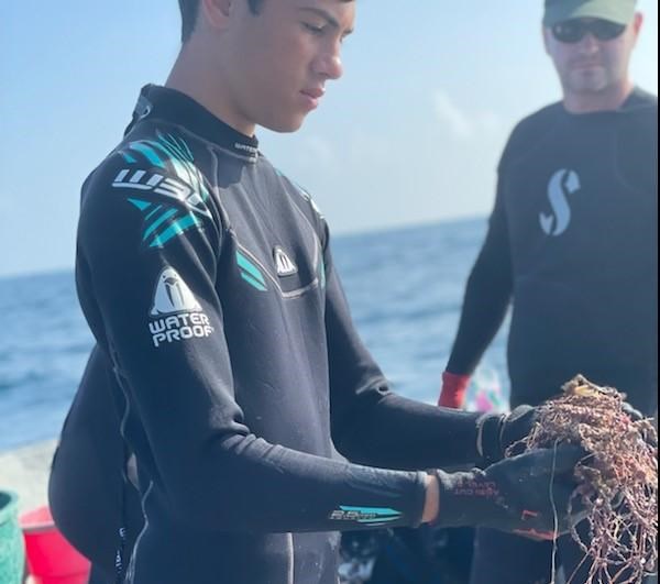 Young man wearing a black wetsuit on a boat with the ocean in the background