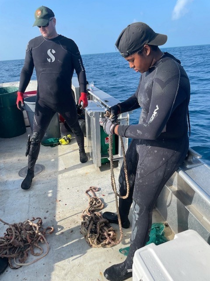 Teenage girl on a boat wearing a wetsuit examining ropes. NPS diver in the background.