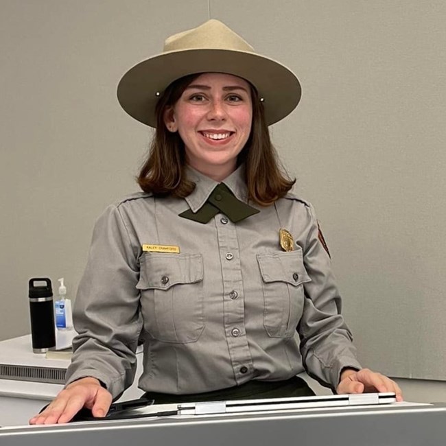 A woman smiles wearing a ranger flat cap and uniform shirt.