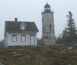 In fog, a white lighthouse tower and small cottage