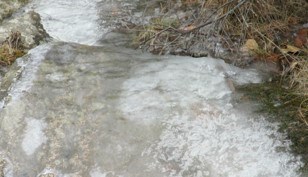 Water flowing under ice coating large rocks along a trail