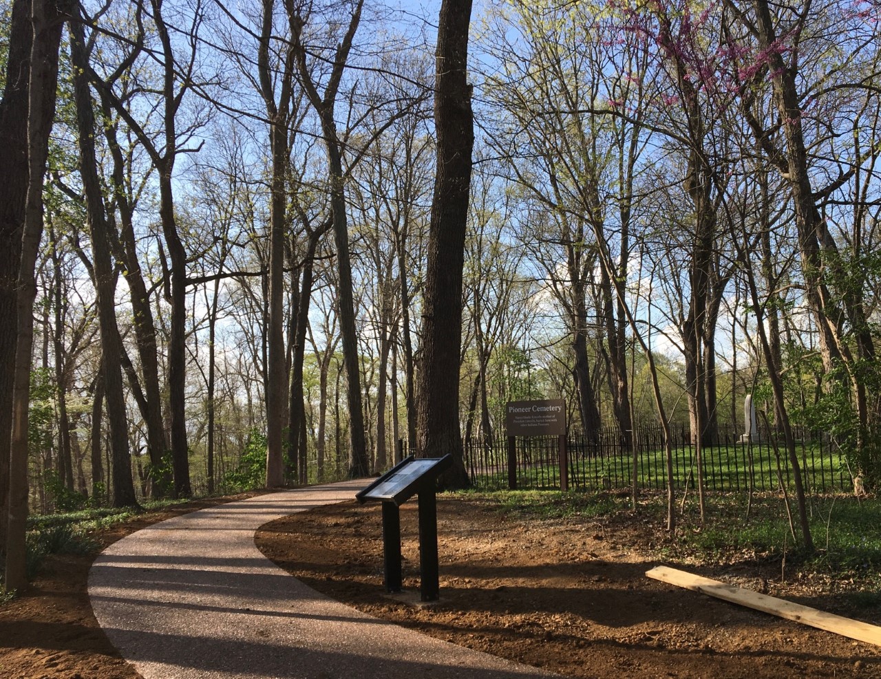 Paved trail curves through woods. Cemetery and wayside to the right.
