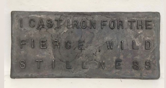Cast iron plaque with the words "I cast iron for the fierce, wild stillness" on it