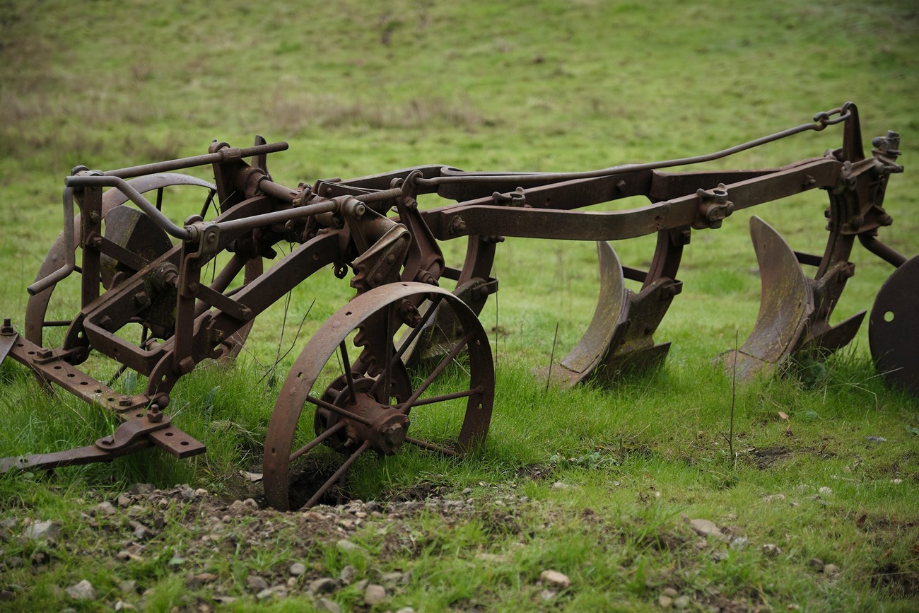 Metal plow with three wheels and two grinders pushing into the ground.