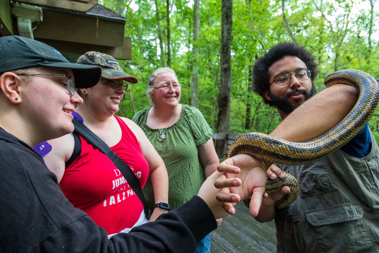 One man stands with a brown snake wrapped around his arms as an audience watches in awe.