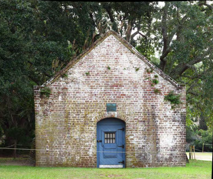 A white washed building of brick with a pitched roof and a blue arched door.