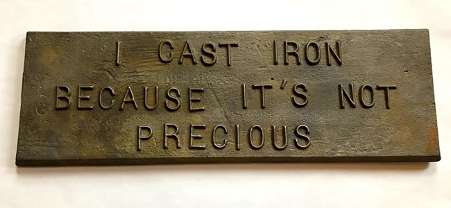 Cast iron plaque with the words " I cast iron because it's not precious" on it