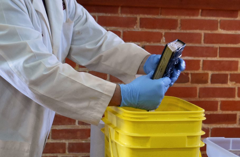 A photograph shows a preservation professional demonstrating how to tightly hold a book closed while rinsing it in a clean water bath.