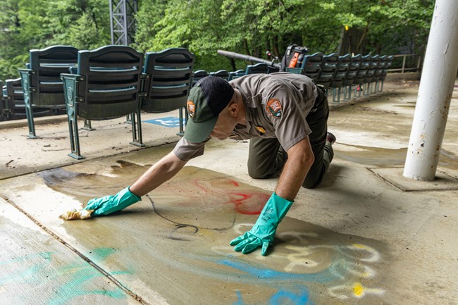 A man in NPS uniform scrubs a concrete floor by hand.