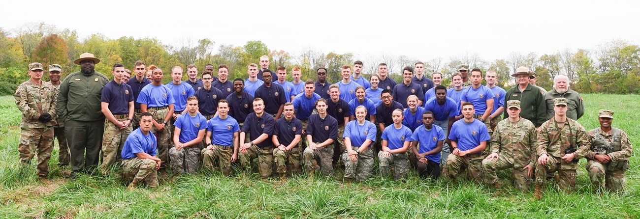 Color photograph of a large group of ROTC cadets in three rows all looking at the camera. They are wearing various shades of blue t-shirts