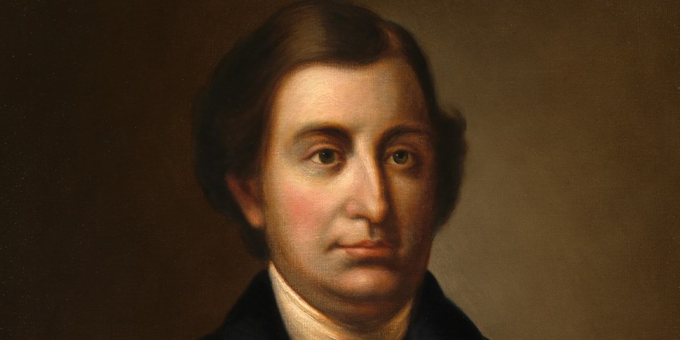 Randolph with dark brown hair parted on right side in black coat.