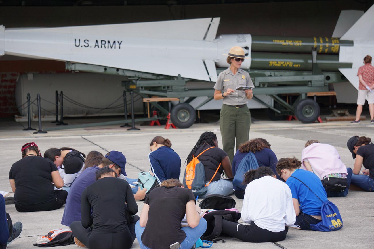 Yvette Cano talked a group of seated kids working on an activity near military equipment