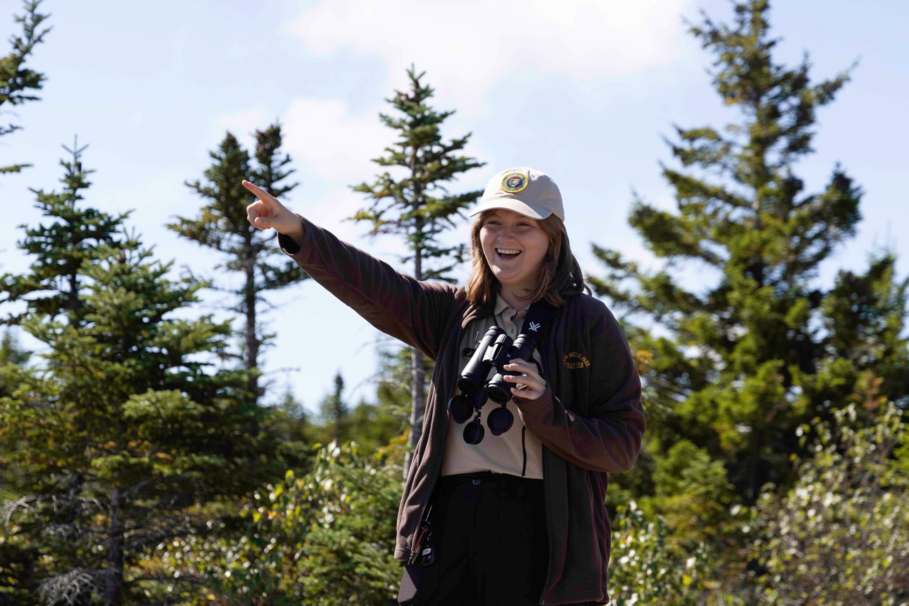 SCA Raptor Intern, Jaz, points and smiles at a bird at the Cadillac Mountain Hawk Watch site.