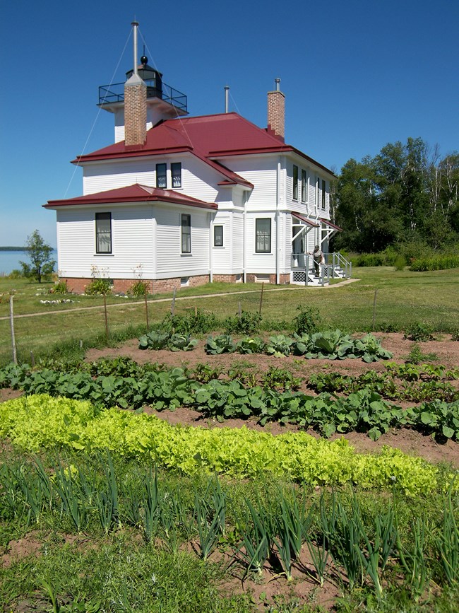 A black and white photo of a white lighthouse and gardens surrounding it.