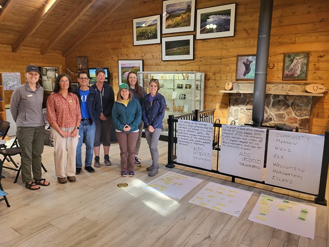 A small group of writers stands next to 3 handwritten posters inside a classroom.
