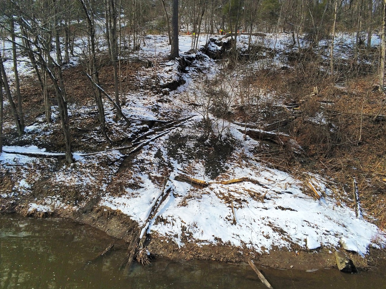 View from the edge of the Delaware River up towards the road showing a big swath of the hillside breaking from the reast of the slope and slumping down into the river.