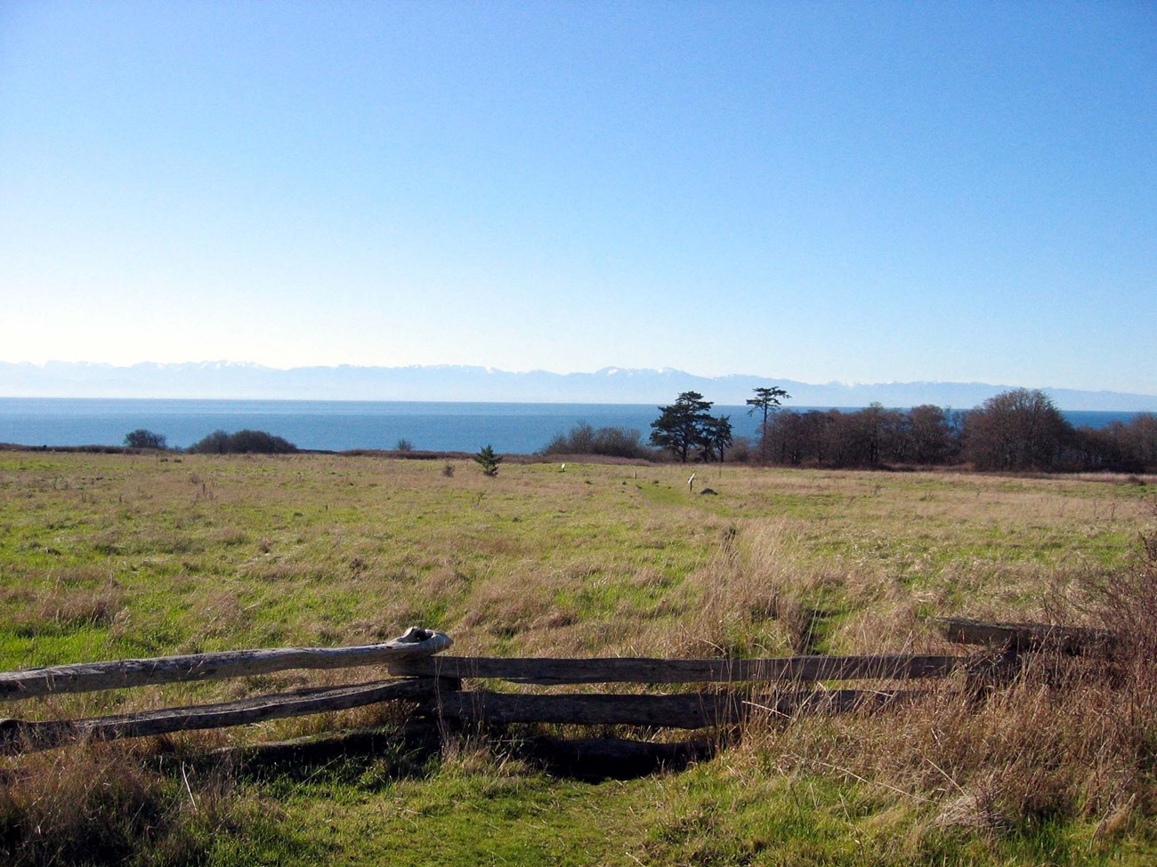 fence in front of prairie with mountains in the distant background