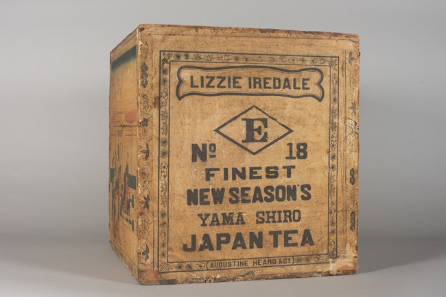 Wooden tea chest covered in a brown paper label with black lettering.
