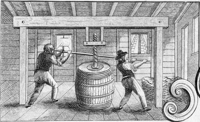 Black and white image of two people packing cod into a barrel.