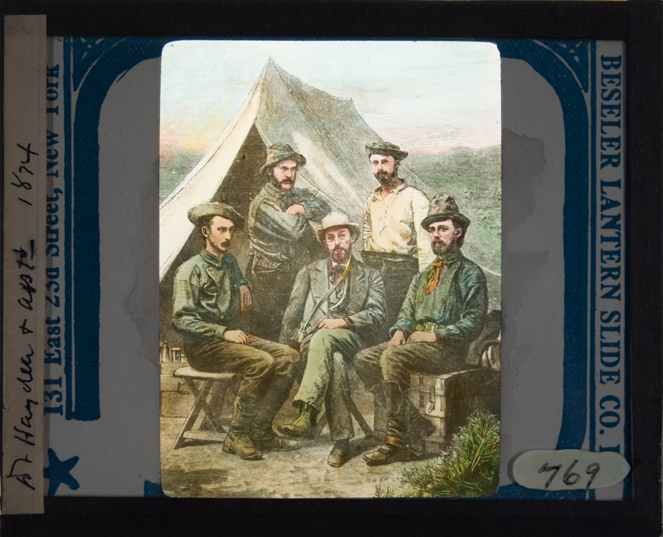 Five men, three seated in front row, two standing behind, are infront of a tent.