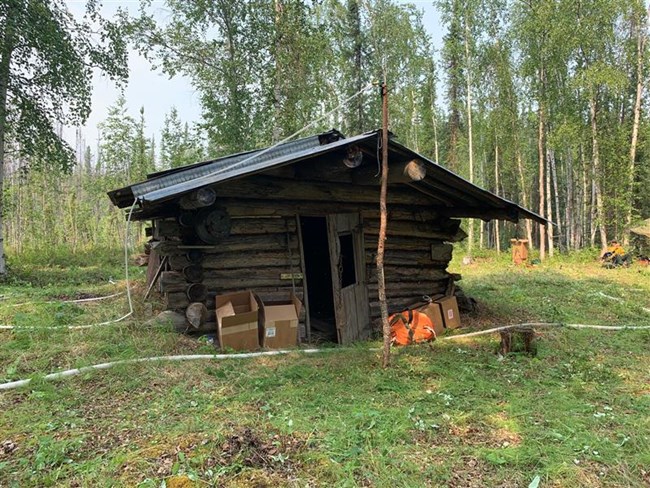 A small log cabin in the woods surrounded by fire equipment and hoses.