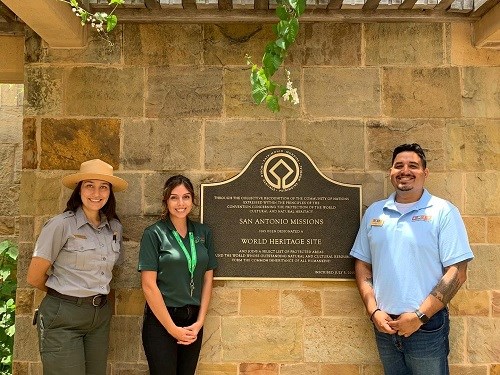 three people posing in front of the san antonio missions sign