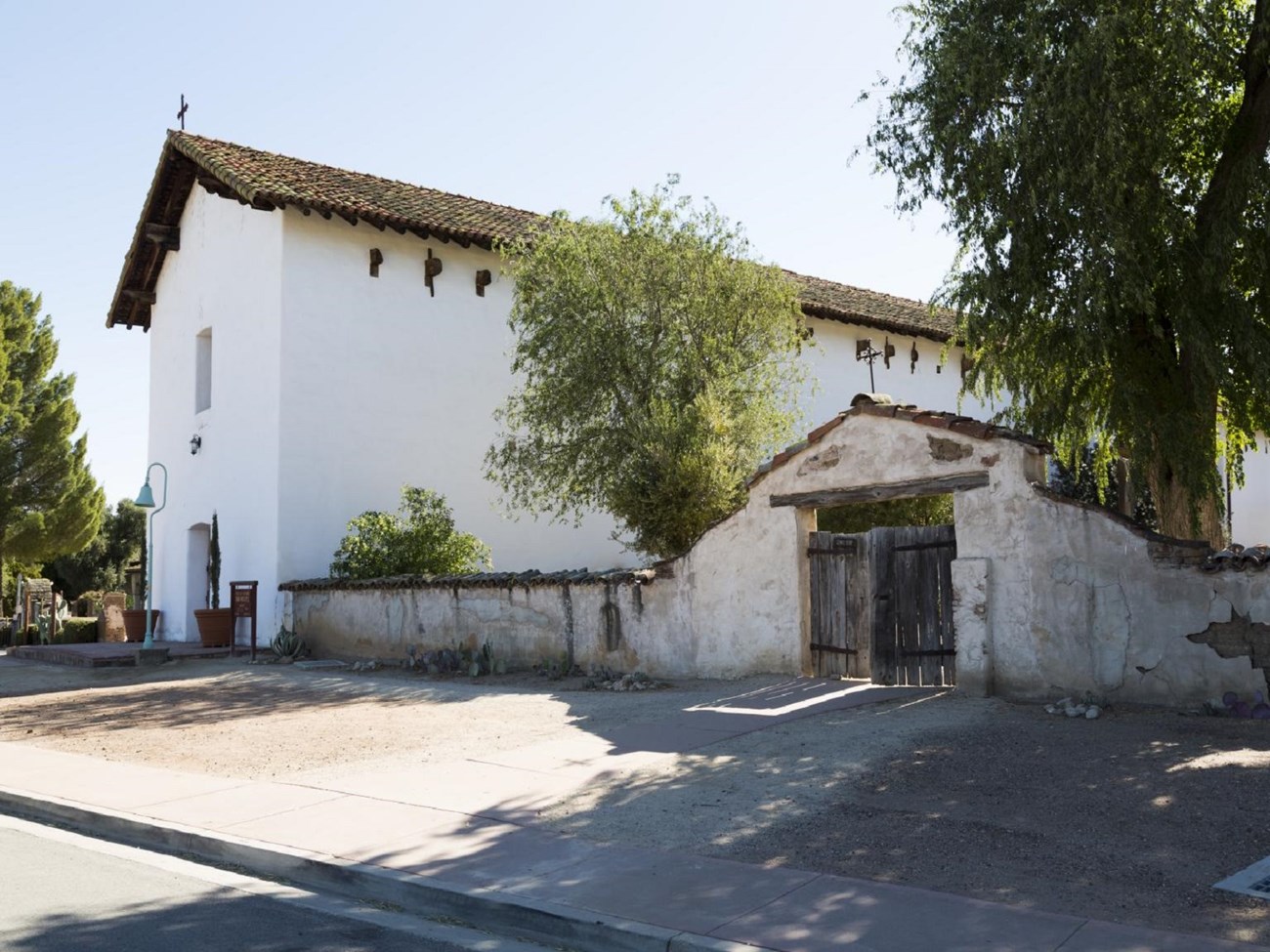 Exterior of white building with brick roof and a white wall with a gate door to the right.