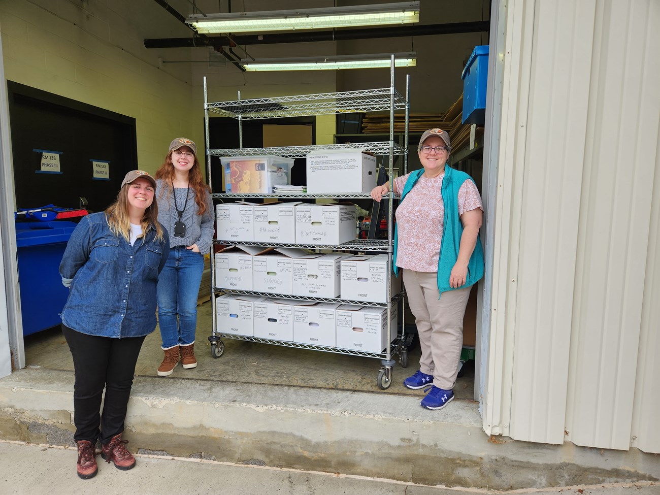 Photograph of 3 people standing next to a rolling shelf with white boxes of files.
