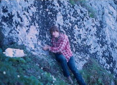 Photograph of a man leaning up against gray, exposed rocks.