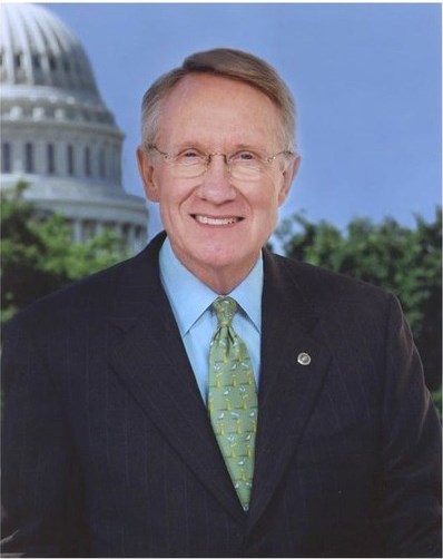 Photograph of a man in a dark colored suit in front of a picture of the US Capitol building
