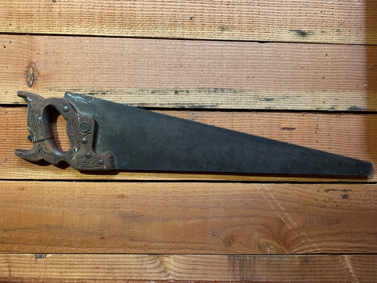 Metal saw with wooden handle hanging on a wall.