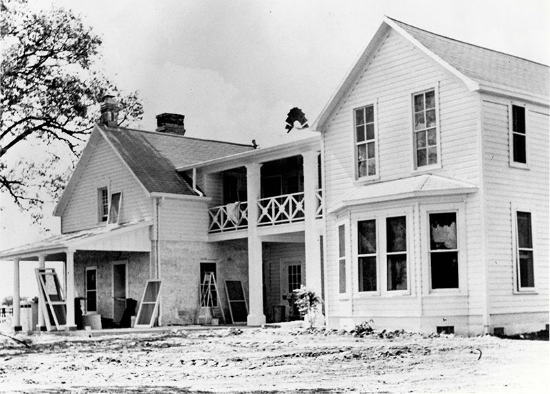 A two-story frame house with assorted building materials in the yard and propped against the house.