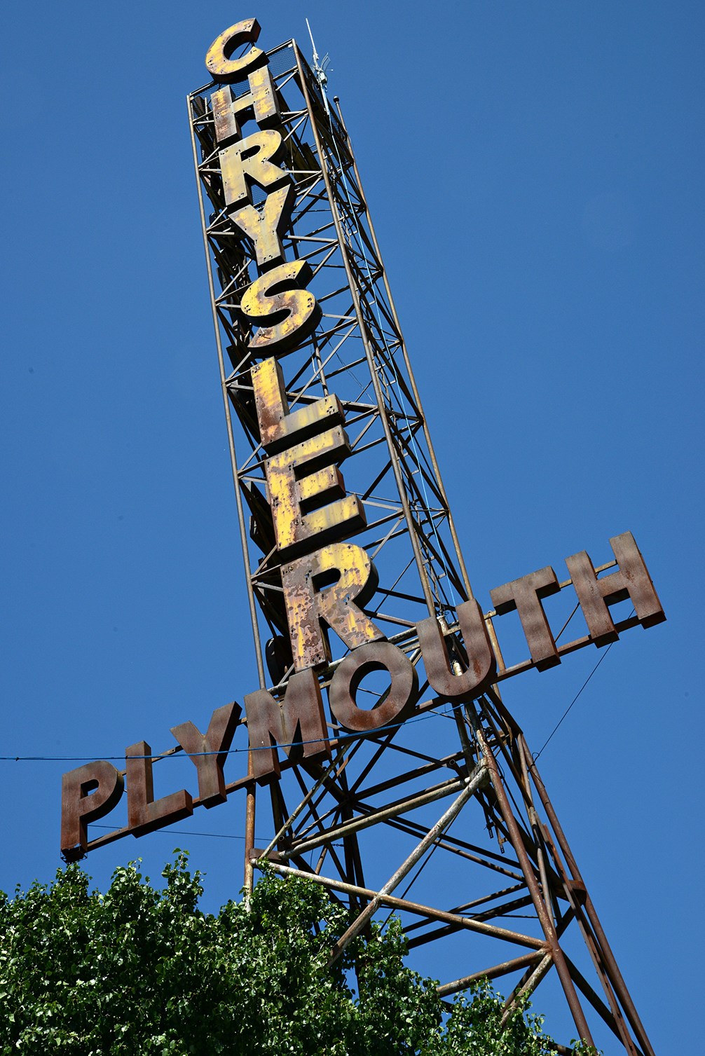 Tall narrow tower made of rods with vertical text reading Chrysler and Plymouth horizontally.
