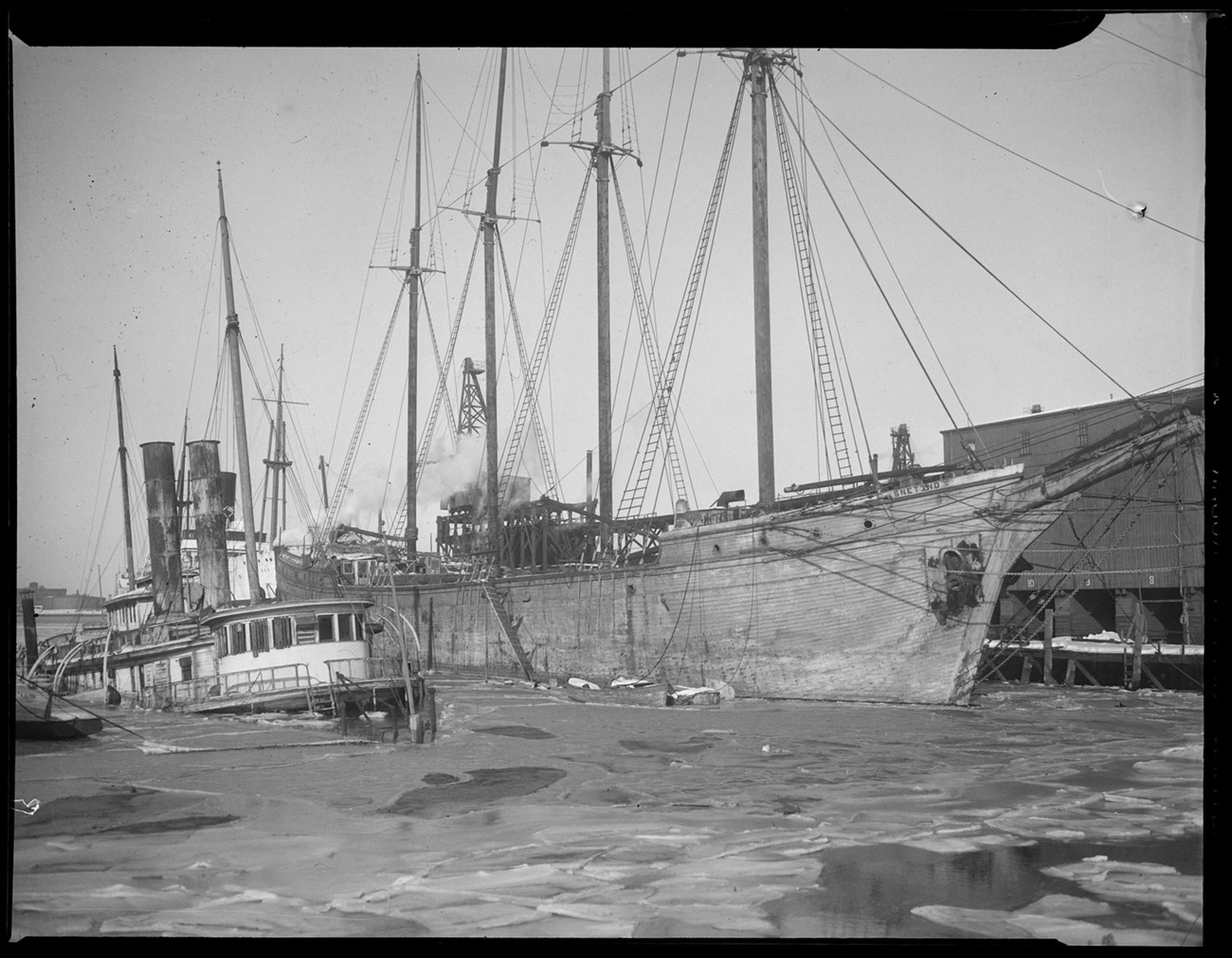 four-masted schooner along a dock with a tugboat next to it