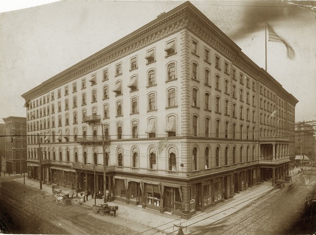 Sepia colored photo of a six-story square building with an American flag in the top right corner.
