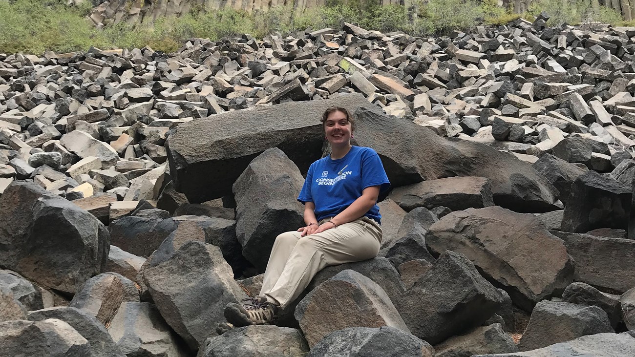 A woman sitting in front of a rock formation.