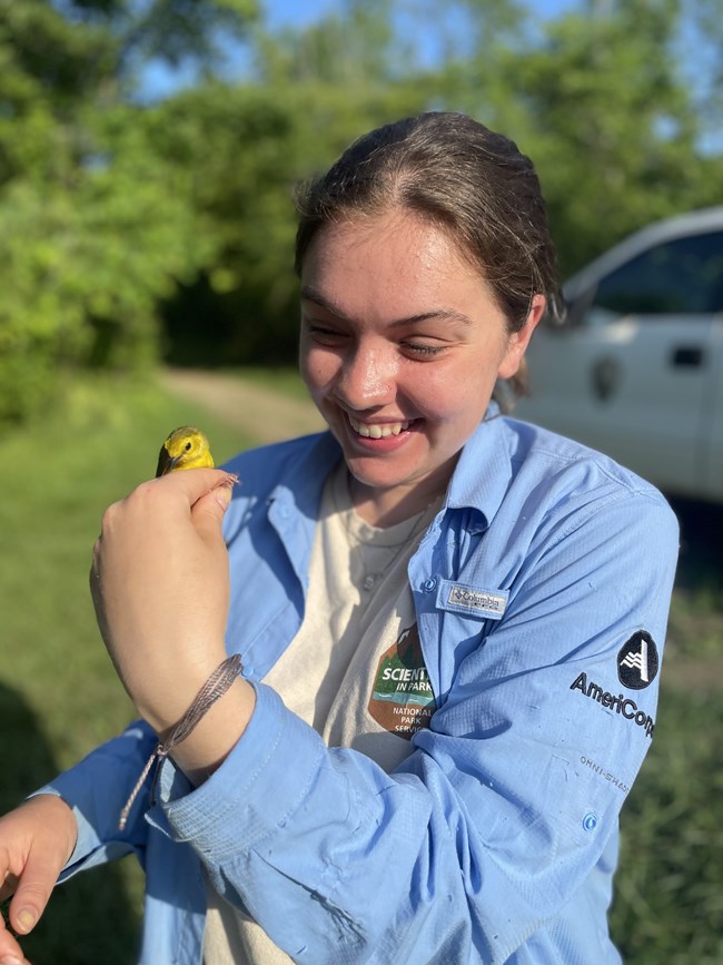A woman wearing a blue AmeriCorps shirt holding a small yellow bird.