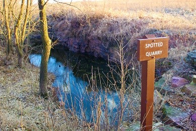 A pit in the prairie with a sign next to it