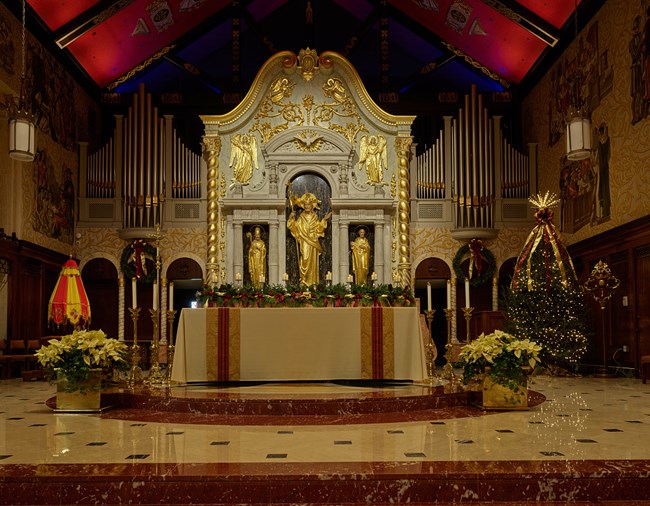 Main altar of the church, three gold statues in the wall behind the altar table and organs on either side of the statues. Altar is decorated for Christmas